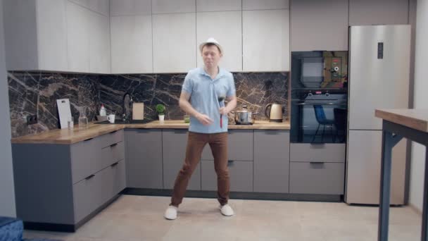 Man heeft plezier in de keuken tijdens het koken, dansen en zingen met een lepel in zijn hand, goed humeur — Stockvideo