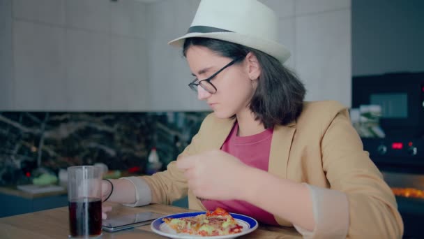 Menina morena bonito em chapéu e óculos, comer e navegar aplicativo móvel — Vídeo de Stock