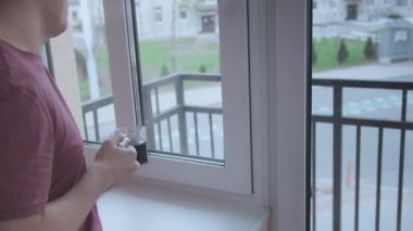Elinde kahve fincanı olan bir adam caddedeki apartmanın penceresinden dışarı bakıyor.