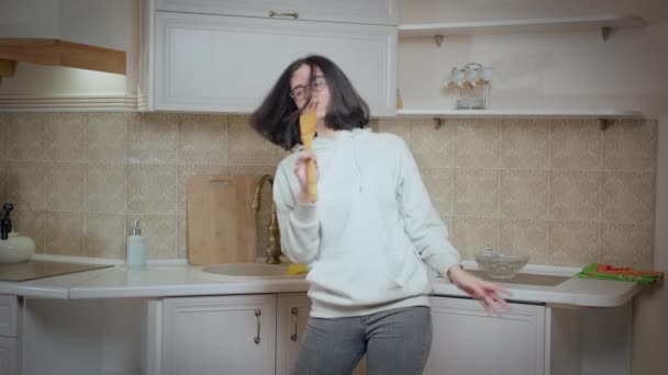 Flicka har roligt dansa och sjunga på bakgrunden av köket hemma, hålla en träsked och sjunga — Stockvideo
