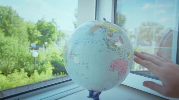 Человек вращает земной шар, который стоит на подоконнике у открытого окна, выбирает маршрут для путешествия — стоковое видео