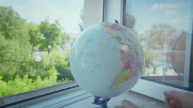 Küre açık bir pencerenin pervazında durur, adamın elleri dünyanın tepesine tıbbi koruyucu bir maske koyar.