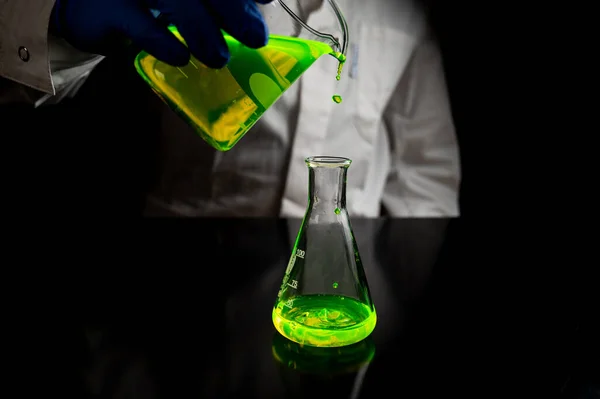 一位研究科学家在黑暗生物医学实验室的玻璃锥形瓶中试验一种绿色荧光滴 以促进医疗护理的发展 复制空间黑色背景 — 图库照片