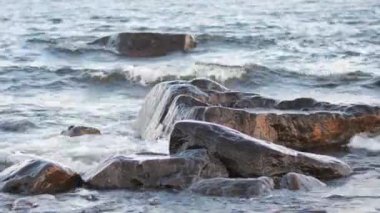 Dev dalgalar beyaz köpükle kayalık deniz kayalıklarına çarpıyor. Su taşların üzerinden akıyor. Deniz kıyısında bol miktarda temiz akarsu. Soğuk su akıntıya karşı yüzüyor. Su arkaplanı kavramı.