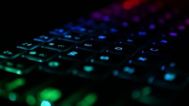 RGB ışıklandırmalı klavye sanal video oyunları için renk değiştiriyor ve karanlık ofis odasındaki güçlü bilgisayarda düzenleme yapıyor. Modern teknolojide gökkuşağı tayfı.
