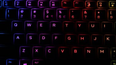 RGB ışıklandırmalı klavye sanal video oyunları için renk değiştiriyor ve karanlık ofis odasındaki güçlü bilgisayarda düzenleme yapıyor. Modern teknolojide gökkuşağı tayfı.