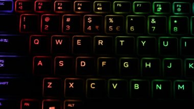 RGB ışıklandırmalı klavye sanal video oyunları için renk değiştiriyor ve karanlık ofis odasındaki güçlü bilgisayarda düzenleme yapıyor. Modern teknolojide gökkuşağı tayfı.