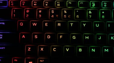 RGB ışıklandırmalı klavye sanal video oyunları için renk değiştiriyor ve karanlık ofis odasındaki güçlü bilgisayarda düzenleme yapıyor. Modern teknolojide gökkuşağı tayfı.