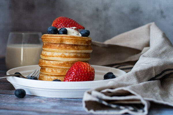 Clear view of Stack of pancakes with honey stick, strawberry, blue berry and whip cream on top in plate, delicious dessert with milk for breakfast.