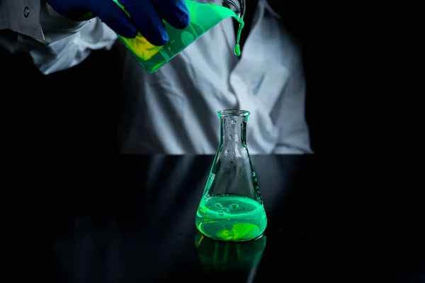 一位研究科学家在黑暗生物医学实验室的玻璃锥形瓶中试验一种绿色荧光滴 以促进医疗护理的发展 复制空间黑色背景 — 图库照片