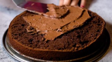 Tanınmayan kadın şekerlemecinin elleri çikolatalı keki masanın üzerinde çikolatalı kremayla süslüyor. 4K, kopyalama alanını kapat Alan derinliği.