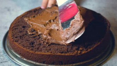 Tanınmayan kadın şekerlemecinin elleri çikolatalı keki masanın üzerinde çikolatalı kremayla süslüyor. 4K, kopyalama alanını kapat Alan derinliği.