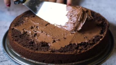 Tanınmayan kadın şekerlemecinin elleri çikolatalı keki masanın üzerinde çikolatalı kremayla süslüyor. 4K, kopyalama alanını kapat Alan derinliği.