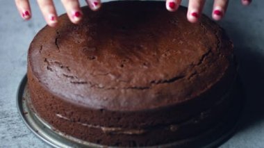 Tanınmayan kadın şekerlemecinin elleri çikolatalı keki masanın üzerinde çikolatalı kremayla süslüyor. 4K, kopyalama alanını kapat Alan derinliği.