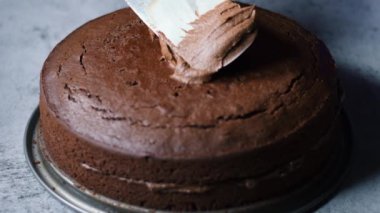 Tanınmayan kadın şekerlemecinin elleri çikolatalı keki masanın üzerinde çikolatalı kremayla süslüyor. 4K, kopyalama alanını kapat Alan derinliği.