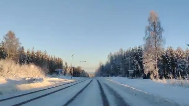 在4K时差的情况下在白雪覆盖的路上开车 清澈的天空 阳光普照在松树顶上 冬季景观下汽车驾驶的超差凸轮视图 — 图库视频影像