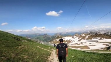 4K 'de yaz tatili dağ doğası panoramik manzara turizmi. İsviçre Alplerinde yürüyüş yapan genç bir adamın macerası çakıllı bir yolda..