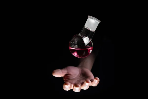 Chemistry round bottom flask dropping on a human scientist hand with black background copy space. Medicinal chemistry red chemical solution and chemical biology. chemisty laboratory and life.