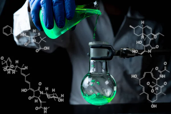 A woman scientist experimenting with a green fluorescent solution in a glass round bottom flask in dark chemistry laboratory for health care medicine development. Copy space black background