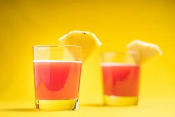ガラスのパイナップルジュースは 夏のビブのためのスプラッシュと滴下液でスライスされた果物の近くに閉じ込めます オレンジの背景に健康的な有機飲料 コピースペース — ストック写真
