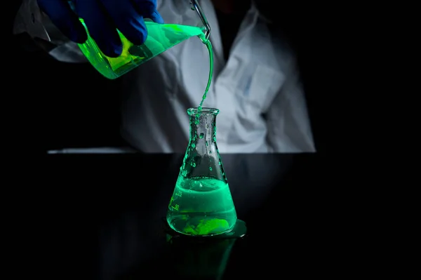 A woman scientist experimenting with a green fluorescent solution in a glass conical flask in dark chemistry laboratory for health care medicine development. Copy space black background