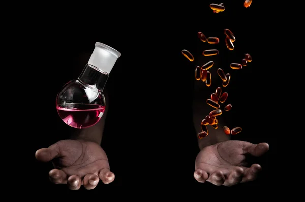 Chemistry round bottom flask and transparent pills dropping on a human scientist hand with black background copy space. Medicinal chemistry red chemical solution and chemical biology. chemisty laboratory and life.