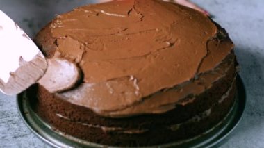 Kadın fırıncı elleri çikolatalı kek pastasını masanın üzerine çikolatalı kremayla süsler. 4K, kopyalama alanını kapat Alan derinliği.