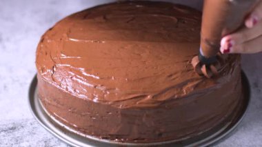 Kadın fırıncı elleri çikolatalı kek pastasını masanın üzerine çikolatalı kremayla süsler. 4K, kopyalama alanını kapat Alan derinliği.