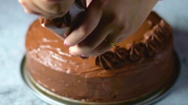 Kadın fırıncı elleri çikolatalı kek pastasını masanın üzerine çikolatalı kremayla süsler. 4K, kopyalama alanını kapat Alan derinliği.