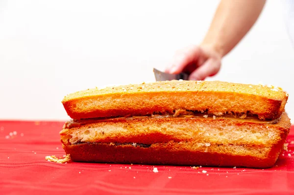 Preparing Cake - Hand cutting stuffed cake on red tablecloth. Isolated on white background with copy space.