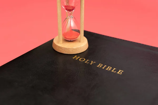 Holy Bible, the Word of God with hourglass. Isolated on red background. Top view. Close-up. Horizontal shot.