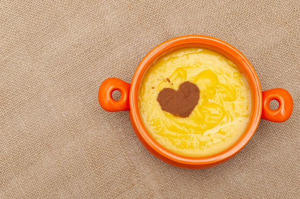 Homemade sweet corn pudding known in Brazil as Curau or Canjica Nordestina in ceramic bowl. Powdered cinnamon in the heart shape. Isolated on jute background. Copy space. Top view.