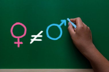 Tebeşir tahtasında cinsiyet eşitsizliği konsepti çiziliyor. El çizgileri eşittir işareti, kadın ve erkeğin sembolü.