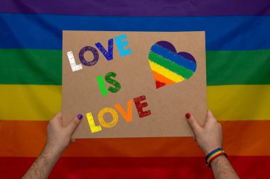 Gökkuşağı arka planında lgbt bayrağı tutan gay adamın elleri