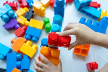 Little boy building tower of block toys sitting on floor in sunny white bedroom. 
