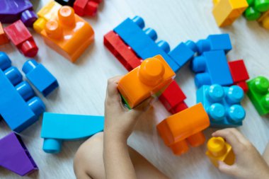 Little boy building tower of block toys sitting on floor in sunny white bedroom.