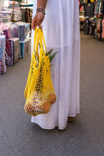Woman in white dress with shopping in reusable cotton net bag at local market, zero waste concept.
