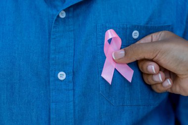 Kadının eli, bir erkeğin göğsüne pembe meme kanseri farkındalığı kurdelesi takıyor.. 