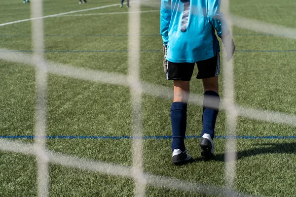 unrecognizable soccer goalkeeper in the goal of the artificial turf soccer field in a children\'s competition.