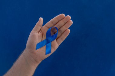 Mavi arka planda prostat kanserini sembolize eden mavi bir kurdele tutan eller..