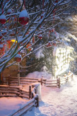 Kış akşamı ve kar yağışı, sokağın aşağısındaki ahşap evin yanındaki ampullerden gelen büyük harfler.