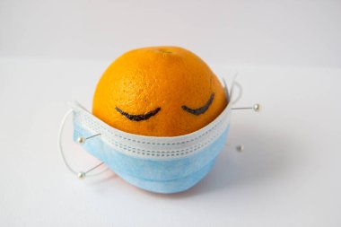 Bir portakala iğneyle tutturulmuş tıbbi maske.