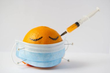 Bir portakala iğneyle tutturulmuş tıbbi maske.