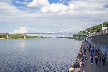Kyiv 'deki Dinyeper Nehri' nin karşısındaki yaya köprüsünde insanlar nehrin kıyısında dinleniyor.