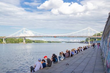 Kyiv 'deki Dinyeper Nehri' nin karşısındaki yaya köprüsünde insanlar nehrin kıyısında dinleniyor.