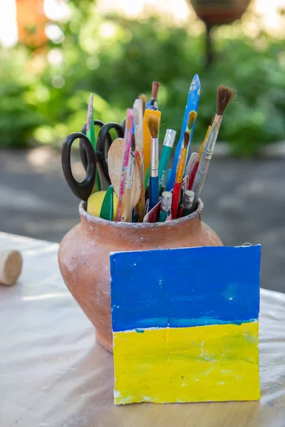 brushes and pencils in a clay pot, flag of ukraine