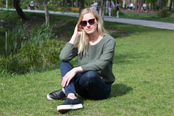 blonde girl in a green sweater sits on the grass