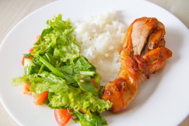 Beyaz tabakta yemek: tavuk budu, pirinç ve salata.