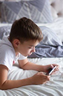 child lying in bed playing on a mobile phone