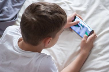 child lying in bed playing on a mobile phone